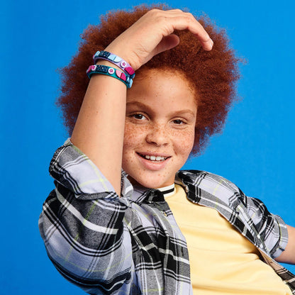 Child showcasing LEGO DOTS Starlight Bracelets with teal and purple tiles against a bright blue background.