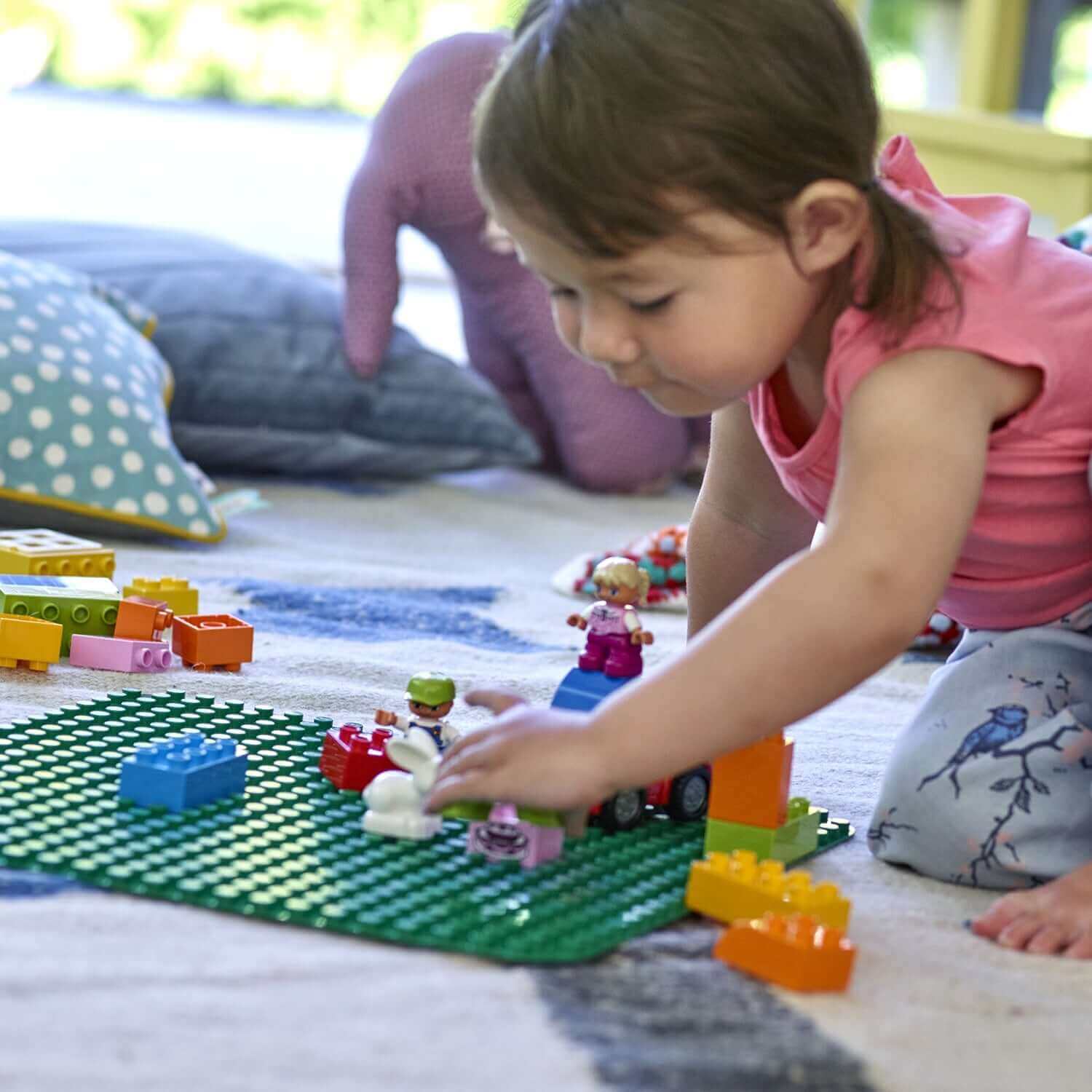 Child playing with LEGO® DUPLO on a green building plate, fostering creativity and imagination.