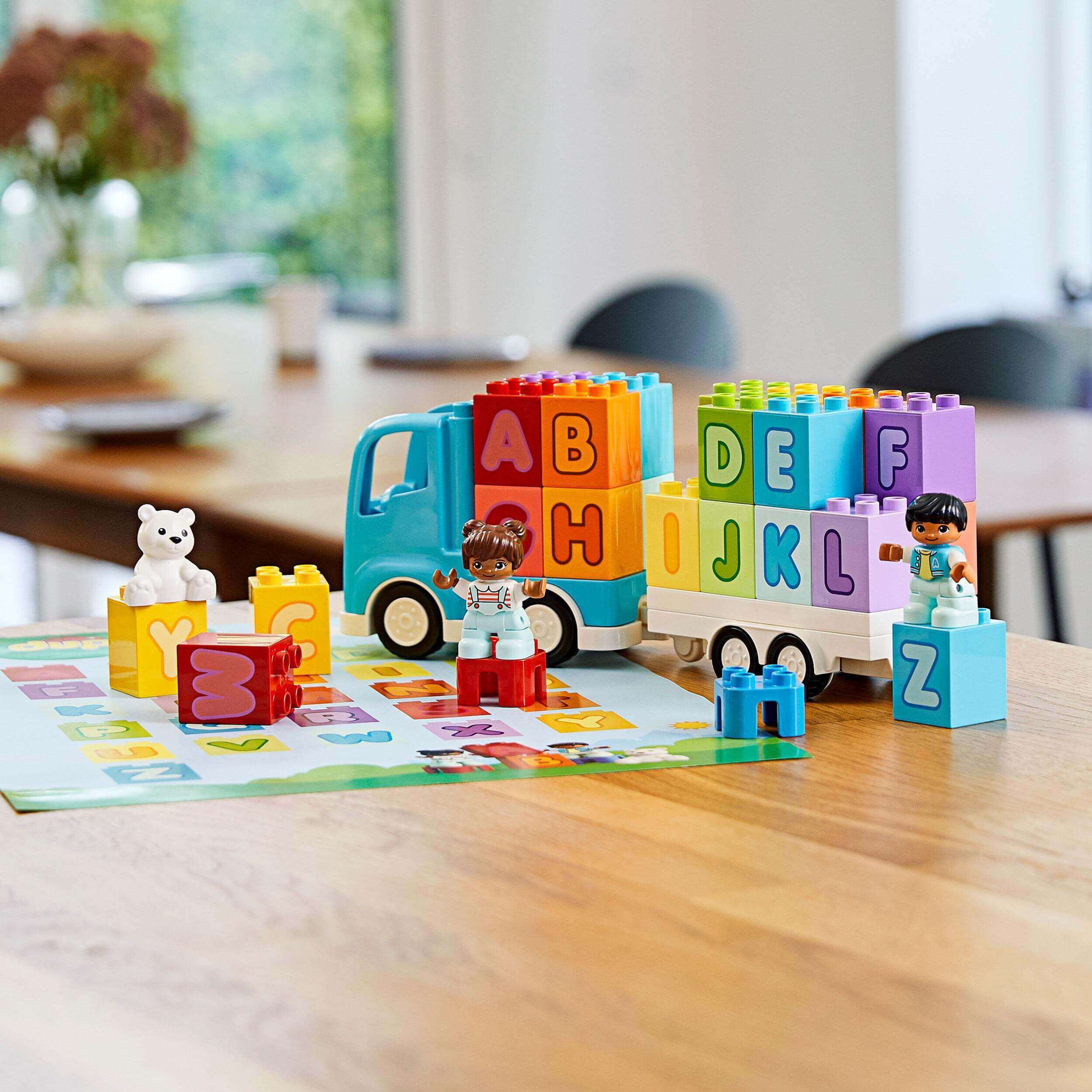LEGO® DUPLO My First Alphabet Truck Set 10915 with colorful blocks, children, and a teddy bear, promoting alphabet learning and play.