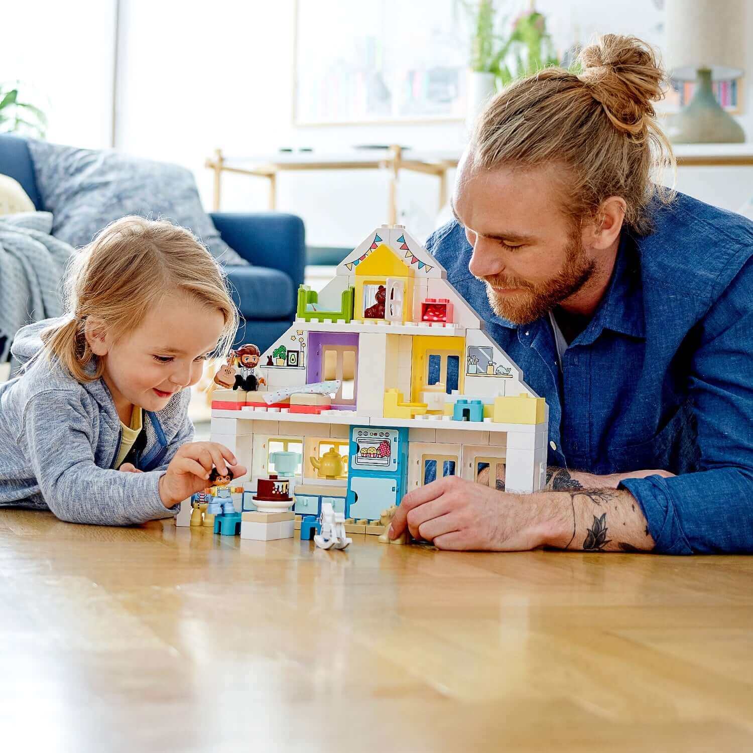 Adult and child playing with LEGO® DUPLO Town Modular Playhouse Set 10929 in a cozy living room.