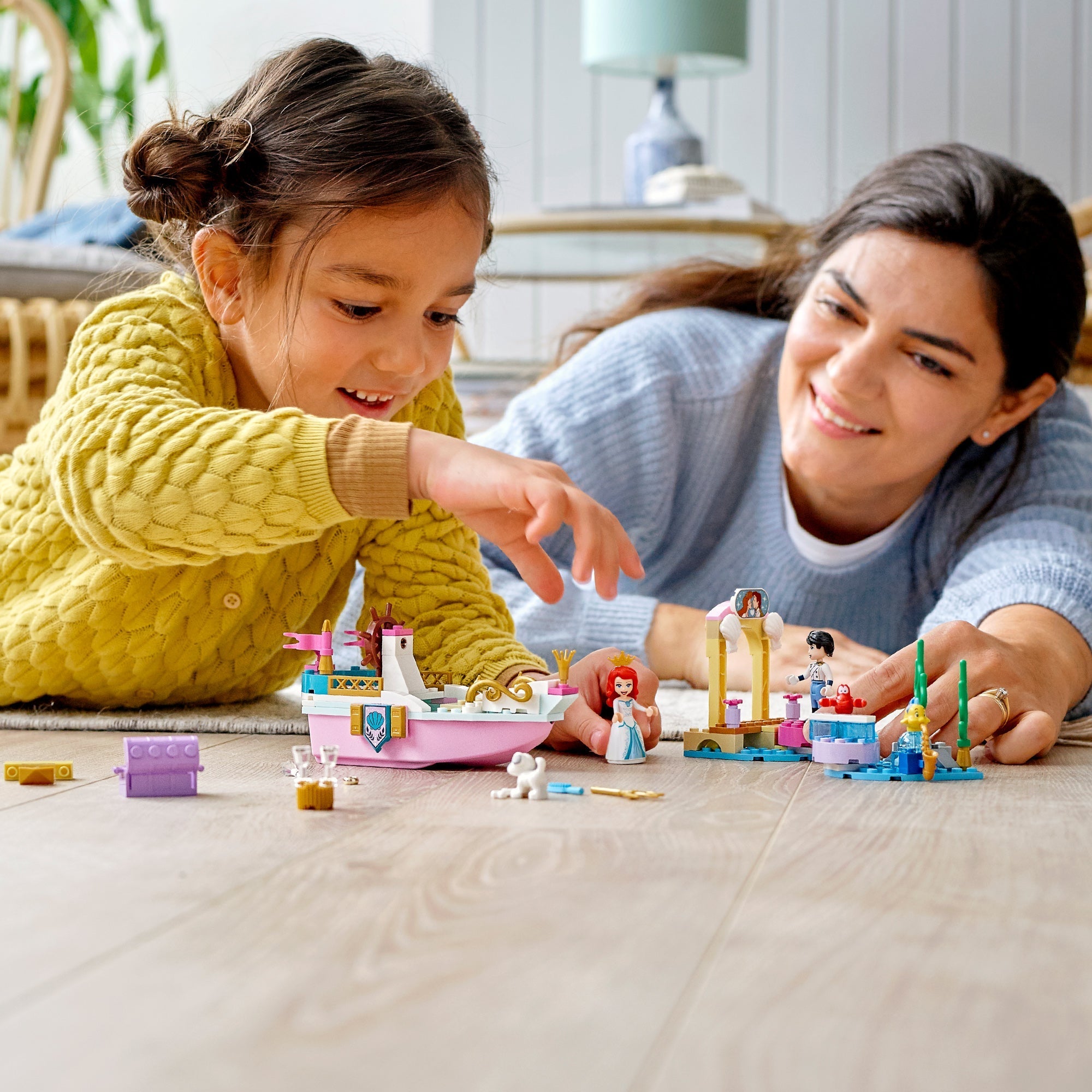 Child and parent playing with LEGO® Disney Ariel's Celebration Boat Toy set on the floor.