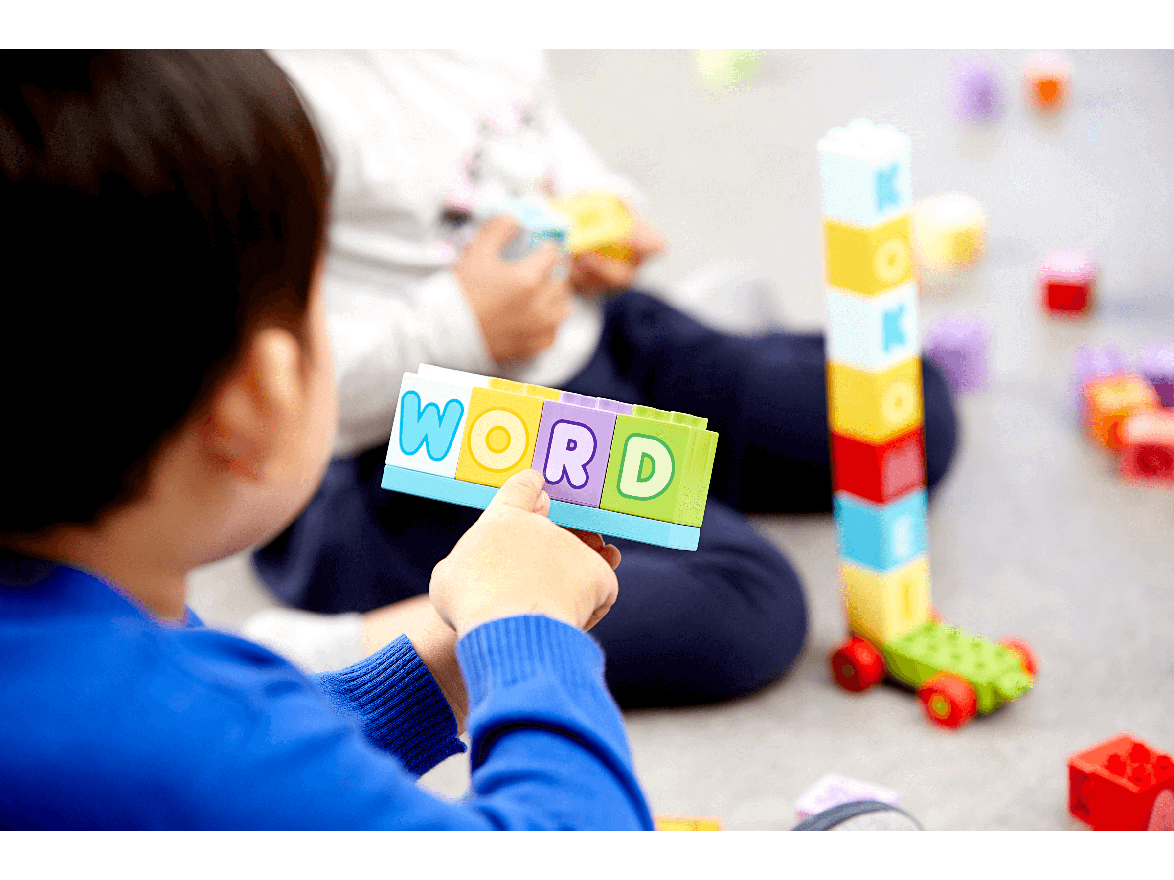 Child playing with LEGO® DUPLO® bricks, spelling the word 'WORD' in colorful letters during learning activities.