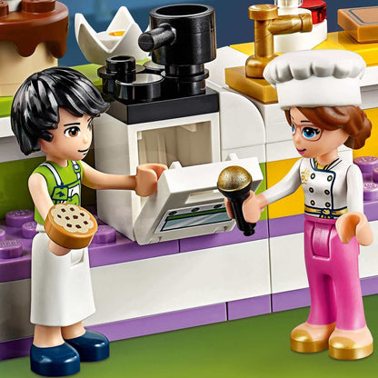 Two LEGO® Friends mini dolls participate in a baking competition, one holding cookies and the other with a microphone.