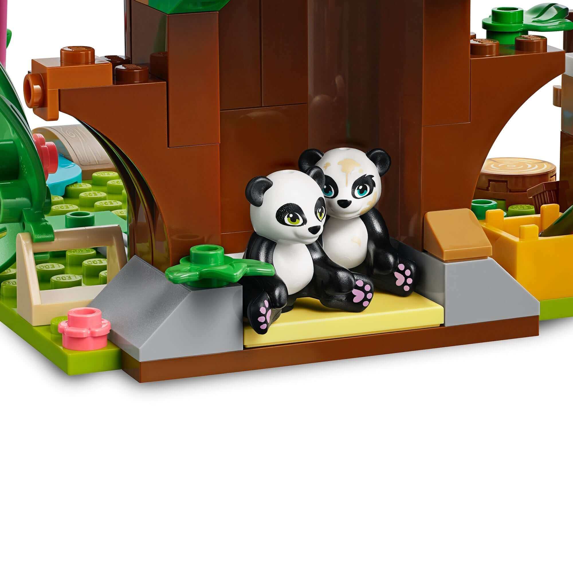 Two cute panda figurines sitting in a LEGO® Friends Panda Jungle Tree House set, surrounded by vibrant jungle elements.