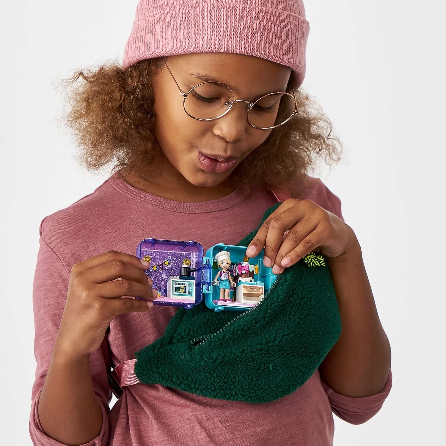 Girl with curly hair opening LEGO® Friends Stephanie's Play Cube Set 41401, featuring baking elements and snacks.