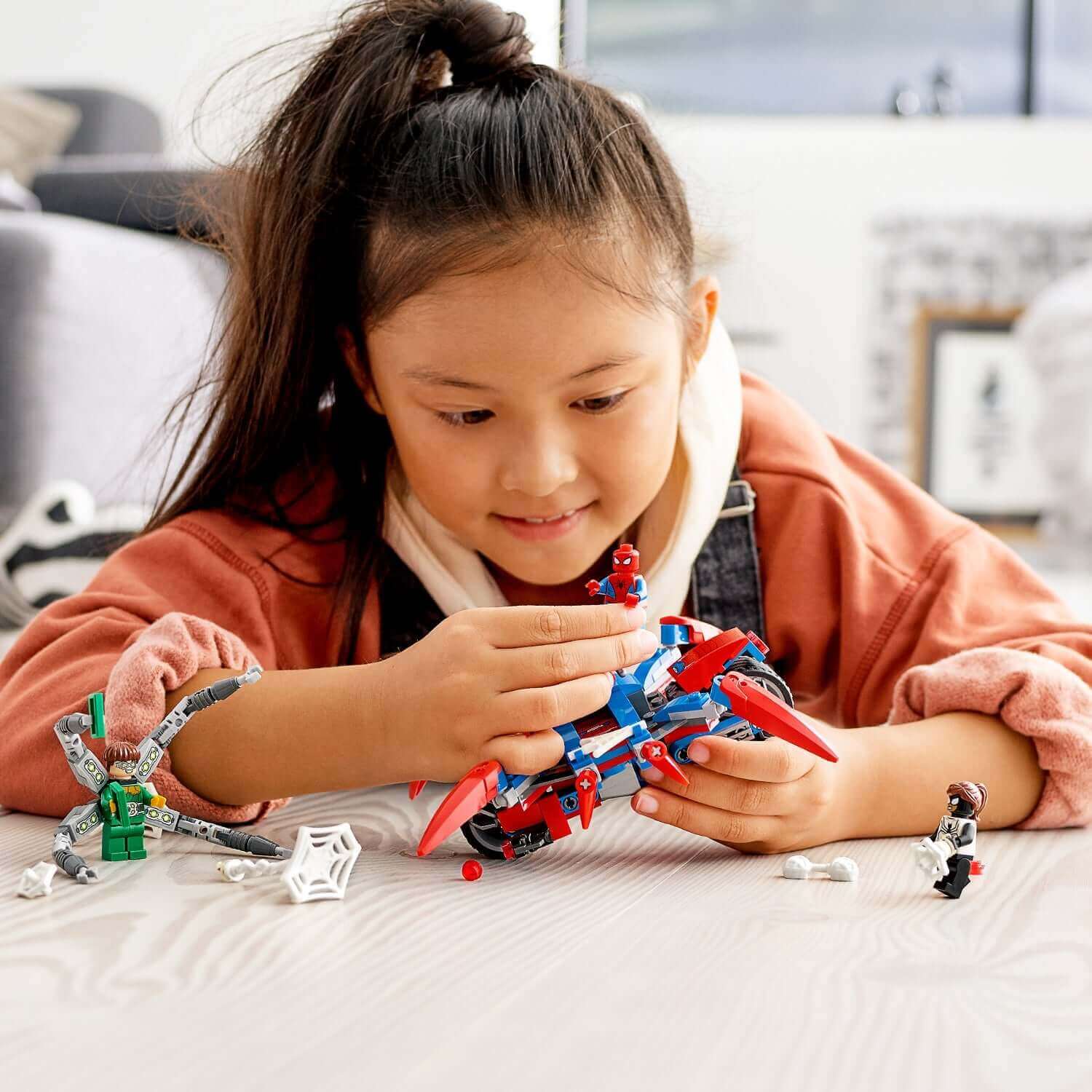 Child playing with LEGO Spider-Man set, including Spider-Man, Doc Ock, and a walking spider.