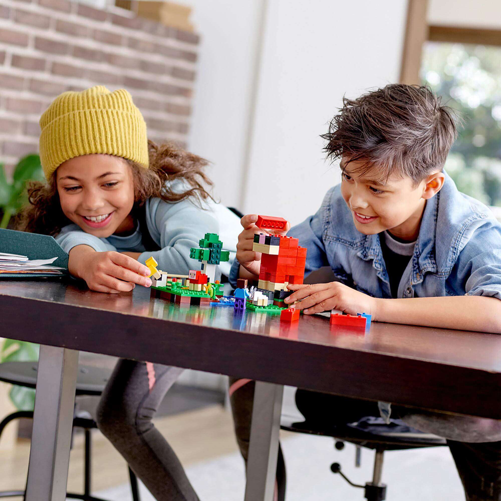 Two kids playing with LEGO® building set, joyfully creating structures and characters at a table.