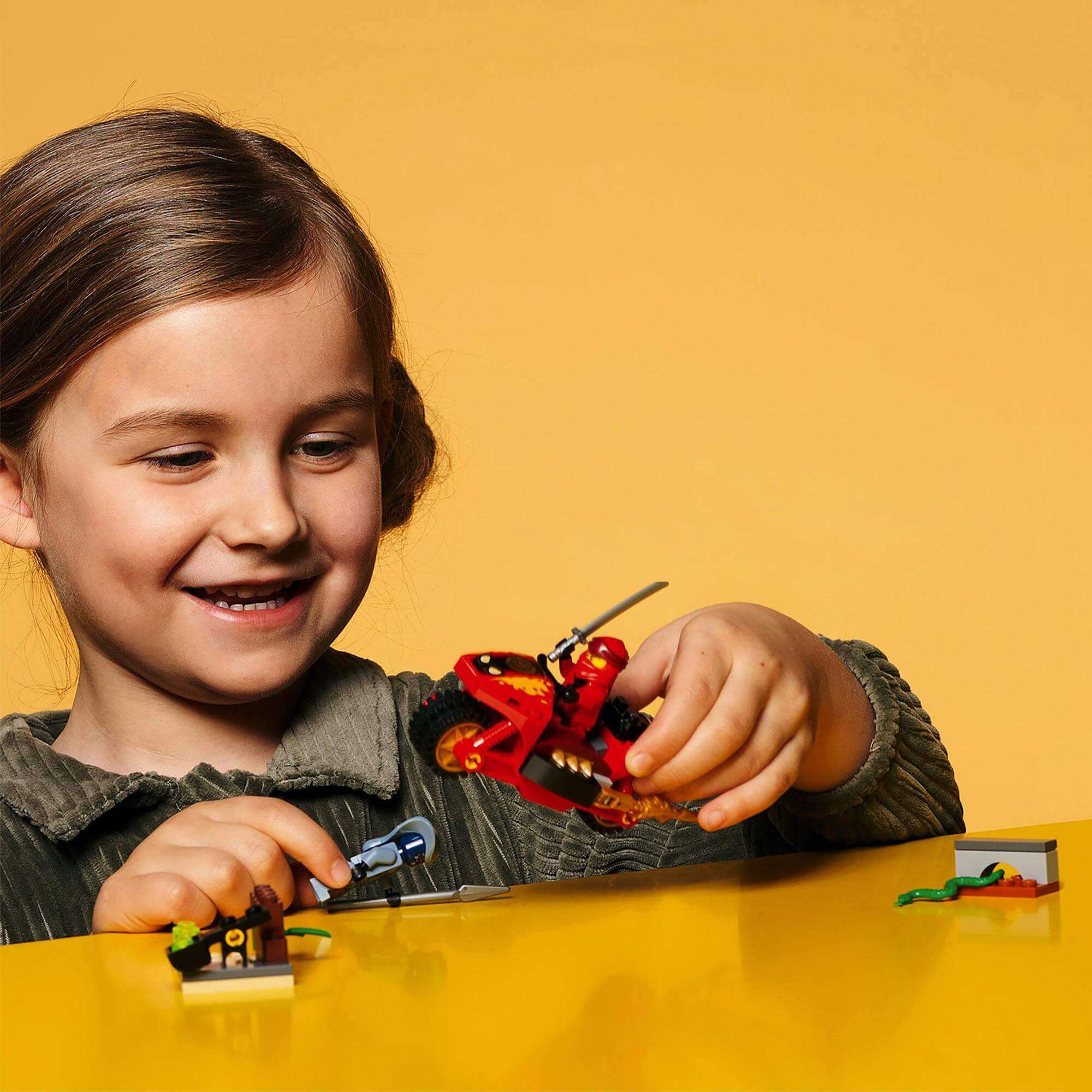 Child enjoying LEGO NINJAGO Legacy Kai’s Blade Cycle Set 71734 with motorcycle toy and minifigures.