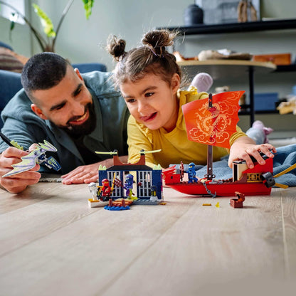 Child and parent playing with LEGO® NINJAGO Destiny’s Bounty Ship set 71749, featuring ship, minifigures, and island.