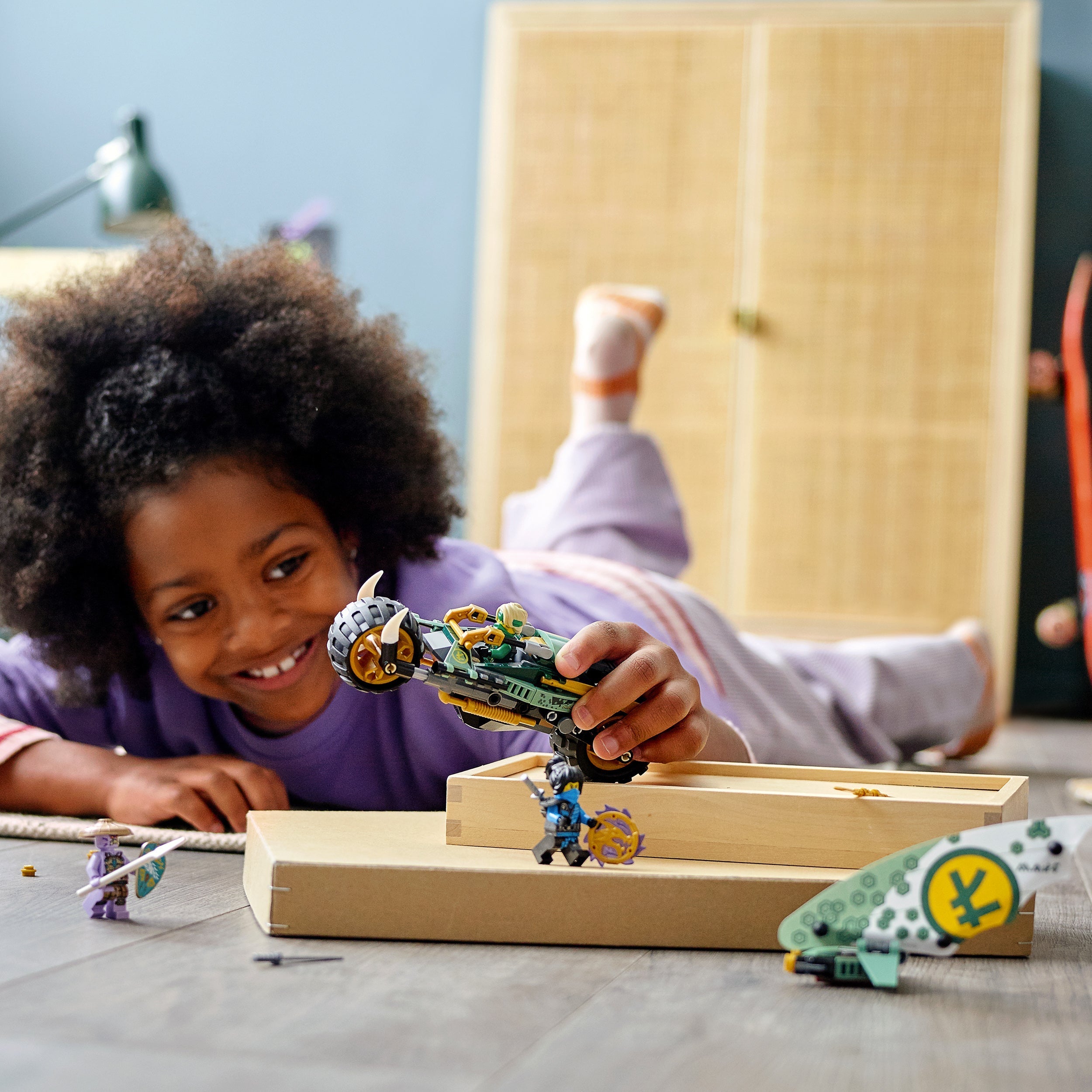 Child playing with LEGO NINJAGO Lloyd’s Jungle Chopper Bike Toy 71745 on the floor, enjoying creative playtime.