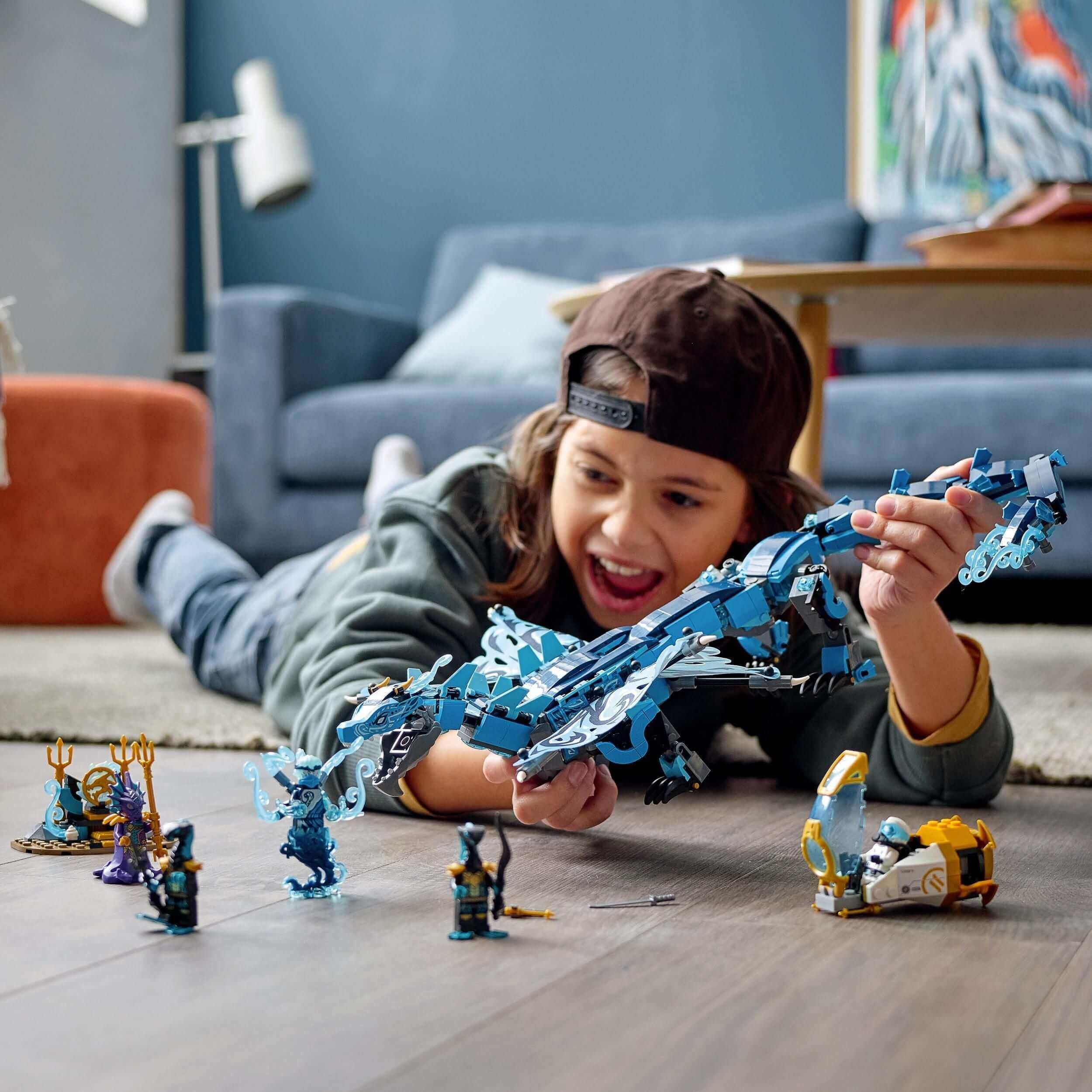Child playing with LEGO® NINJAGO Water Dragon set 71754, featuring a dragon, submarine, and minifigures on the floor.