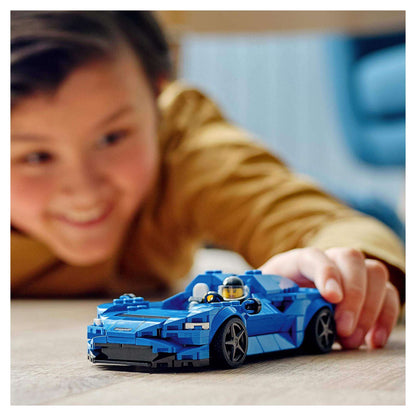 Child playing with LEGO® Speed Champions McLaren Elva model toy 76902 on a wooden surface, showcasing fun and creativity.