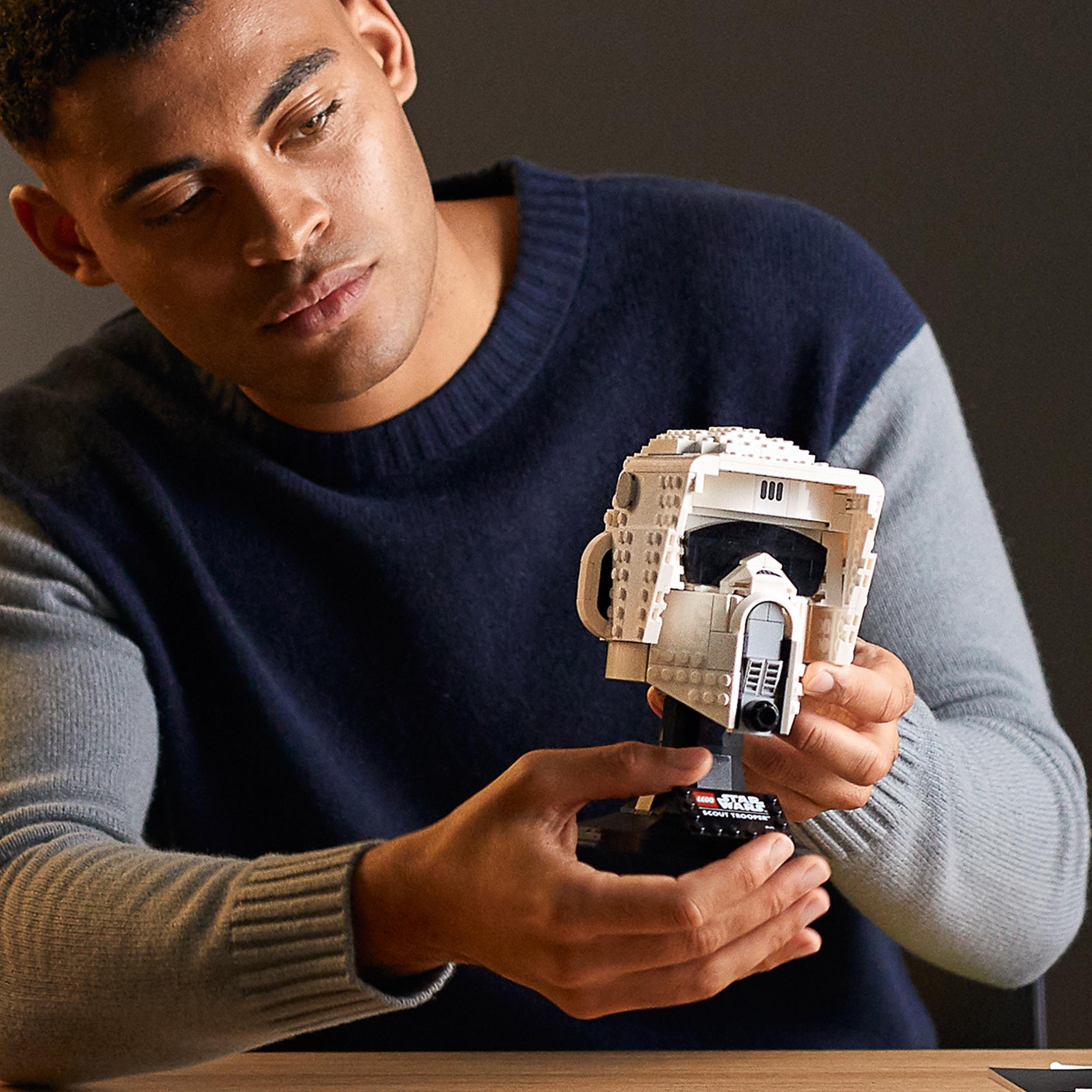 Man holding a detailed LEGO® Star Wars Scout Trooper Helmet model, showcasing adult collectibles.