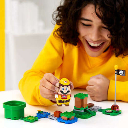 Child in a yellow sweater interacting with LEGO® Super Mario™ Builders set and Power-Up Pack, smiling with Mario figure.
