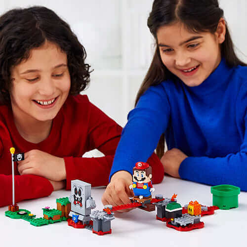 Two children enjoying the LEGO® Super Mario™ Whomp's Lava Trouble Expansion Set 71364, playing with Mario figure.