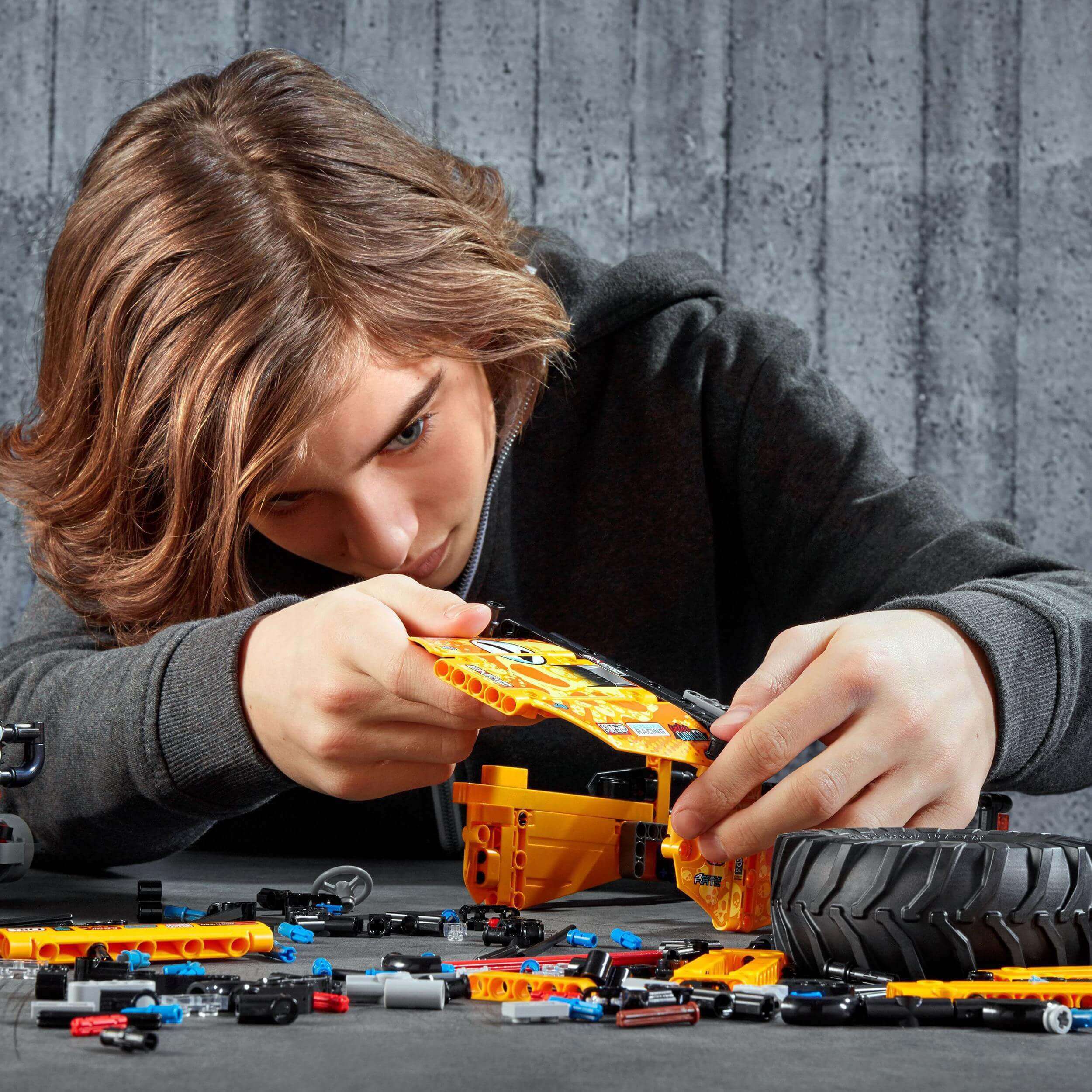 Child building LEGO Technic 4x4 X-treme Off-Roader with colorful pieces and tires on workspace.