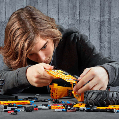 Child building LEGO Technic 4x4 X-treme Off-Roader with colorful pieces and tires on workspace.