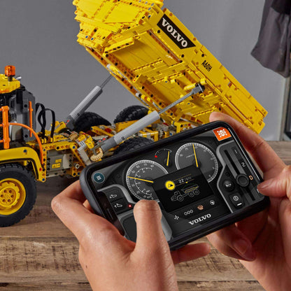 Person controlling a LEGO® Technic 6x6 Volvo Articulated Hauler Truck 42114 using a smartphone app.
