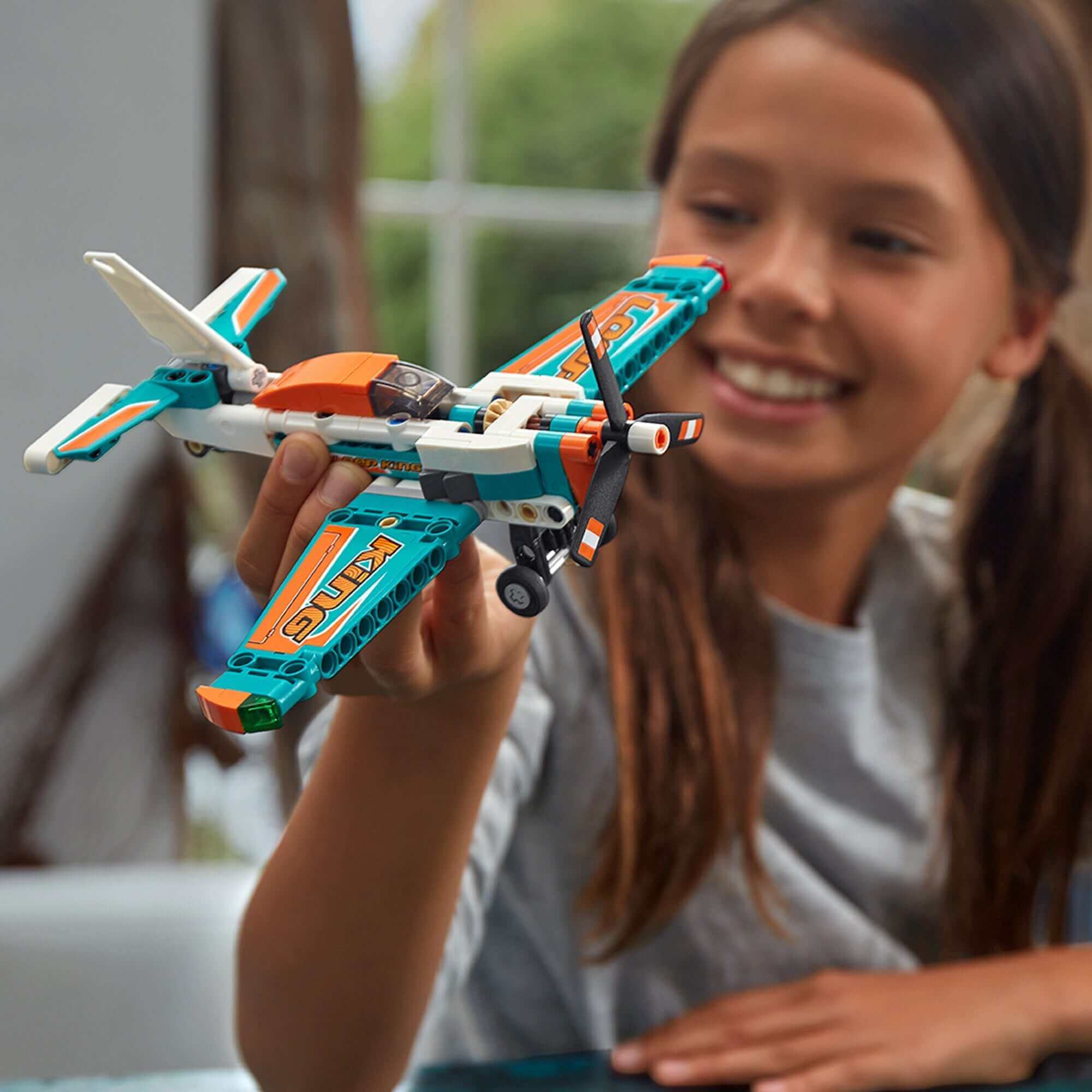 Child holding LEGO® Technic Race Plane Jet 42117 with spinning propeller indoors, showcasing creativity and play.