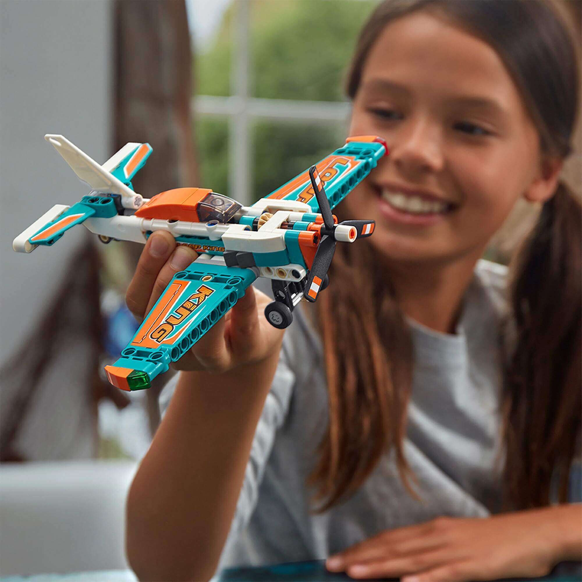 Child holding LEGO® Technic Race Plane Jet 42117 with spinning propeller, excitedly playing indoors.