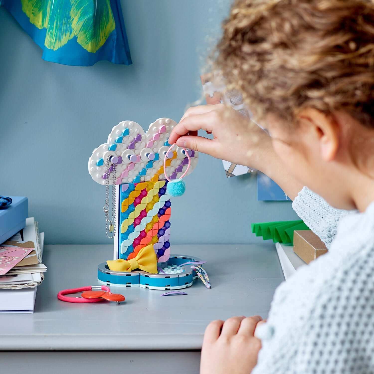 Child placing jewellery on the DOTS Rainbow Jewellery Stand Set by LEGO® 41905, showcasing creative DIY design.