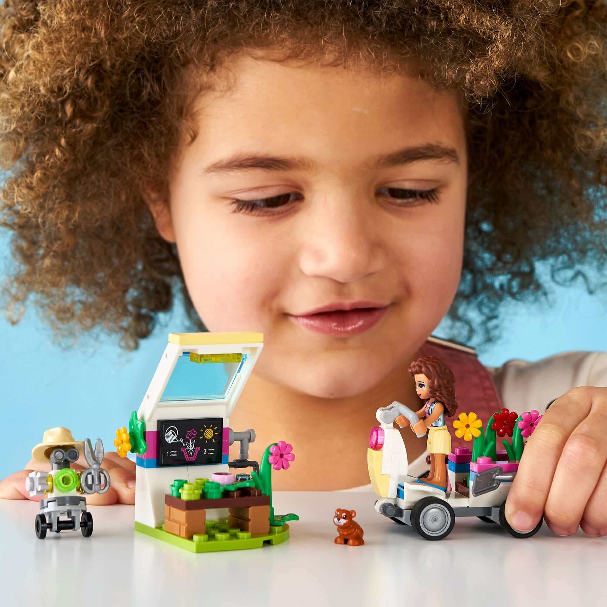 Child playing with LEGO® Friends Olivia's Flower Garden set featuring a greenhouse and gardening accessories.
