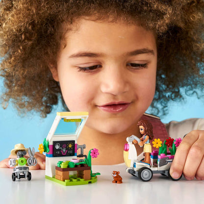 Child playing with LEGO® Friends Olivia's Flower Garden set featuring a greenhouse and gardening accessories.
