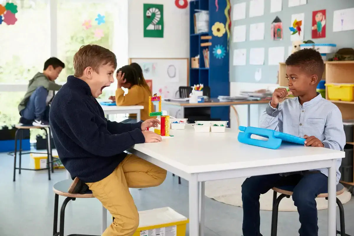 Two young boys playing in a classroom, one laughing and the other focused on a tablet, encouraging collaboration and creativity.