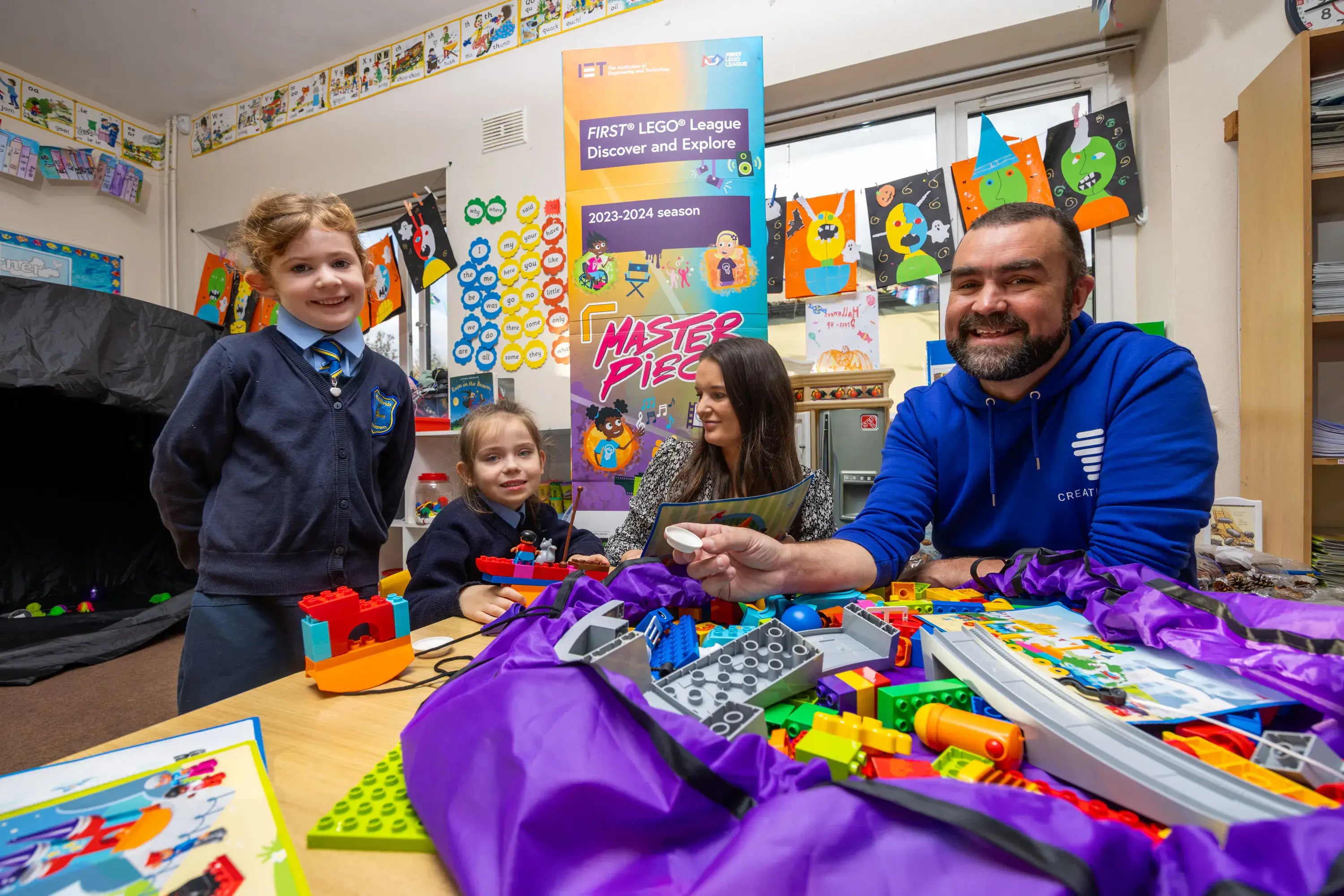 Children and a mentor engaging with LEGO in a classroom during the FIRST LEGO League event.