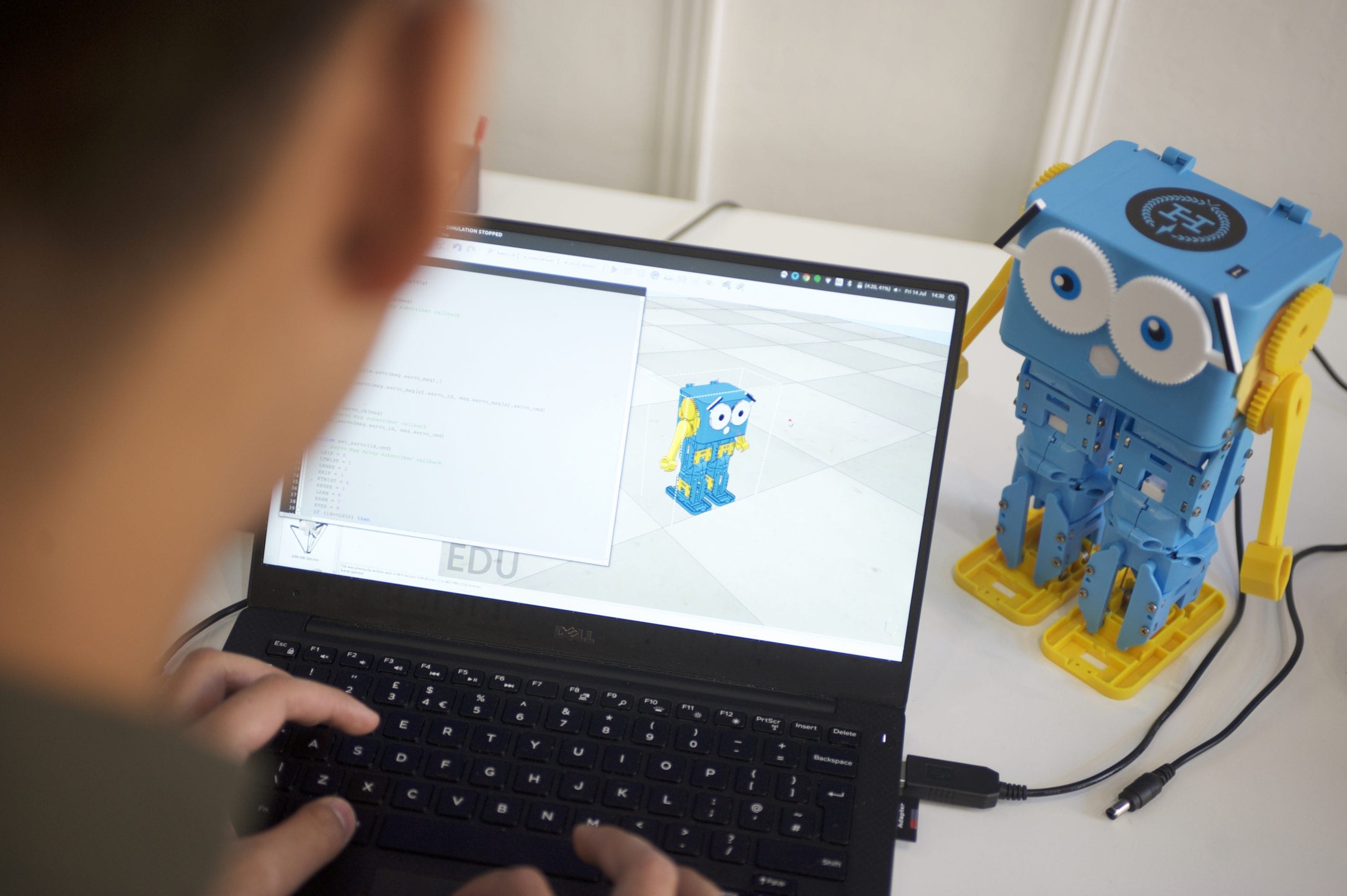 Child programming on laptop with Robotical Marty V2 walking robot educational toy beside it.