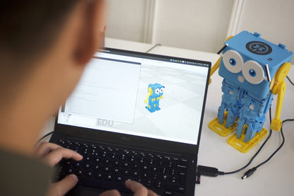 Child programming on laptop with Robotical Marty V2 walking robot educational toy beside it.
