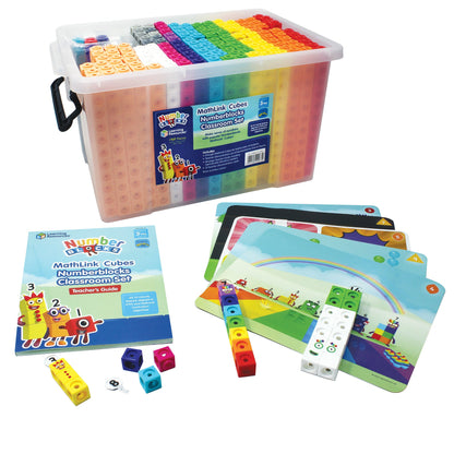 A high-angle product shot of the MathLink® Cubes Numberblocks® Classroom Set on a white background. A large, clear plastic storage tote with a black handle is filled with hundreds of organized, multi-colored cubes. In front of the tote lies an 88-page Teacher’s Guide, several large, double-sided activity mats featuring colorful Numberblocks scenes, and various MathLink cubes snapped together with Numberling character faces attached. Small, individual loose cubes and a Numberling "8" piece are scattered near