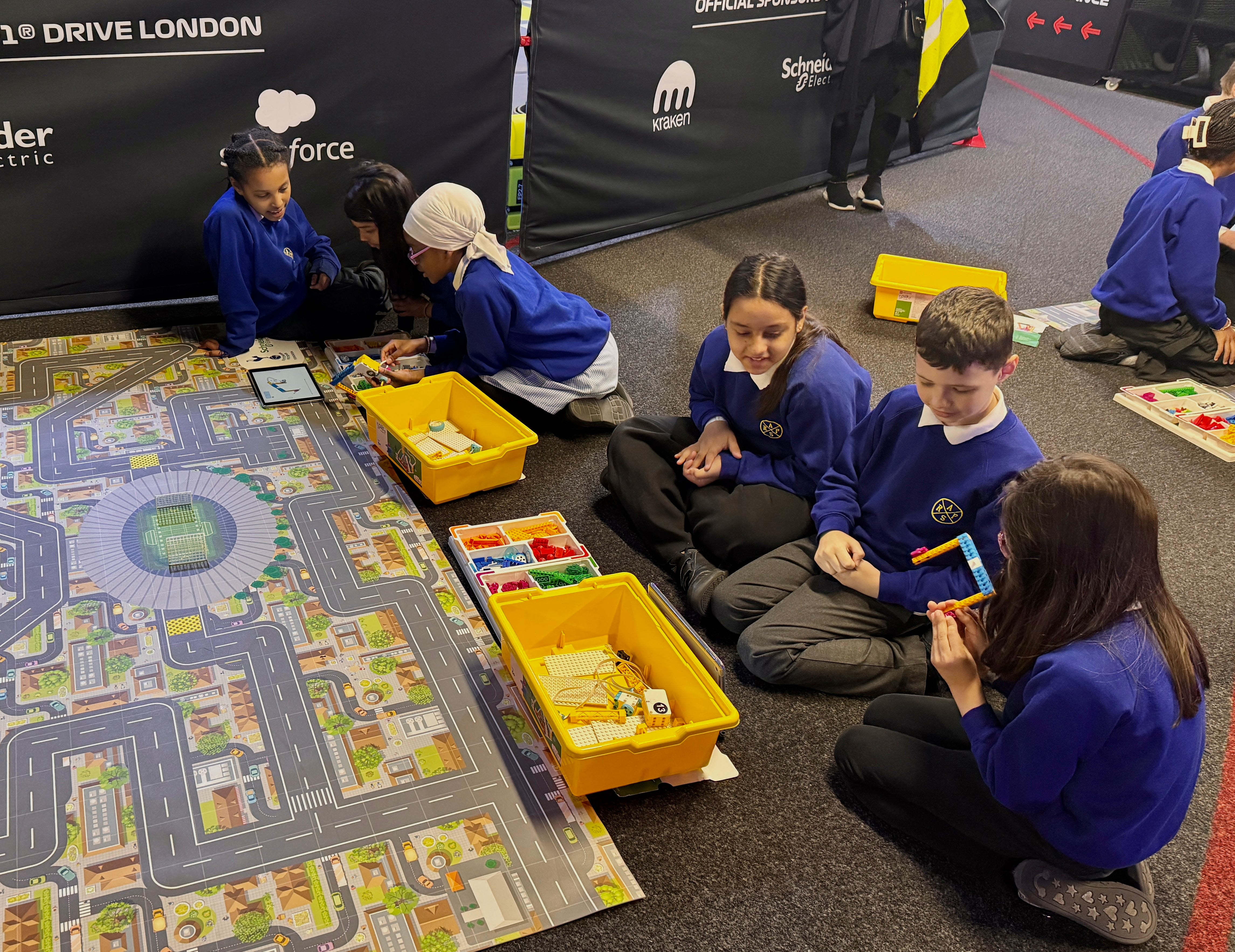 Students engaged in a STEM activity, building models on a colorful road map with LEGO blocks.