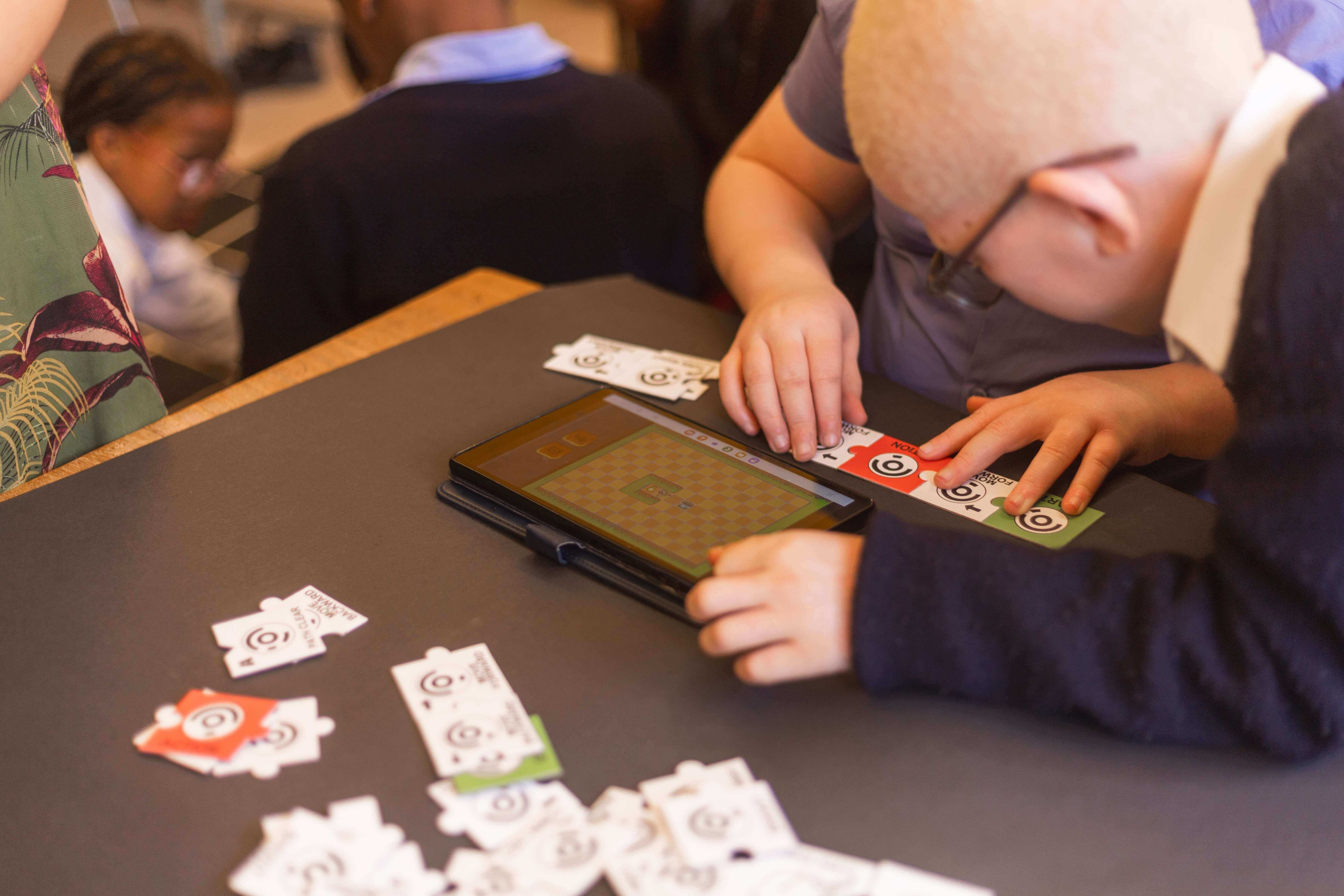 Children playing a board game on a tablet, focused on cards on a black table top.