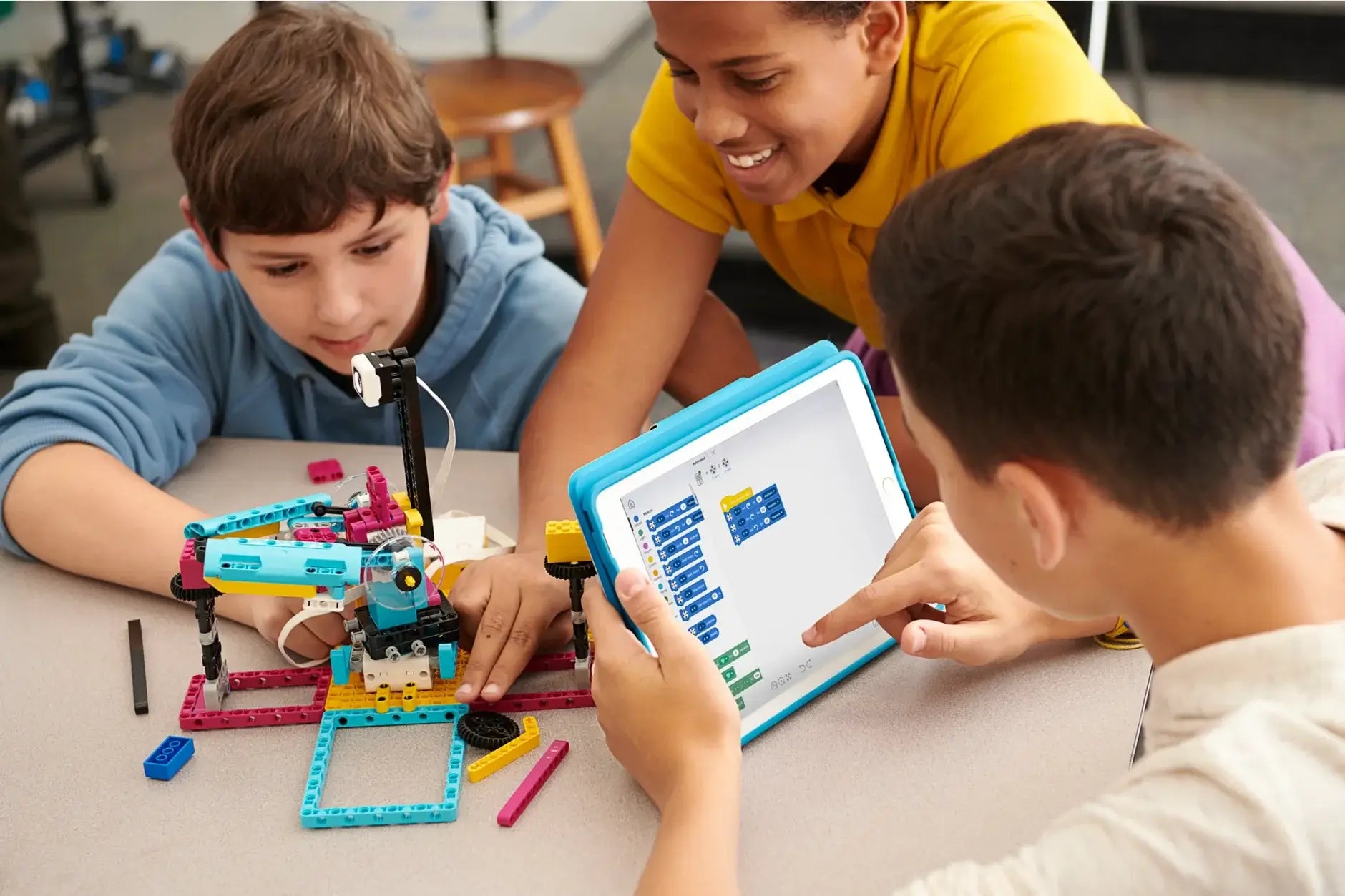Three children engaged in a hands-on robotics activity, programming their creation using a tablet.