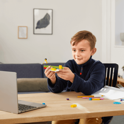 Child engaging with LEGO® Education BricQ Motion kit at home, using laptop for learning.