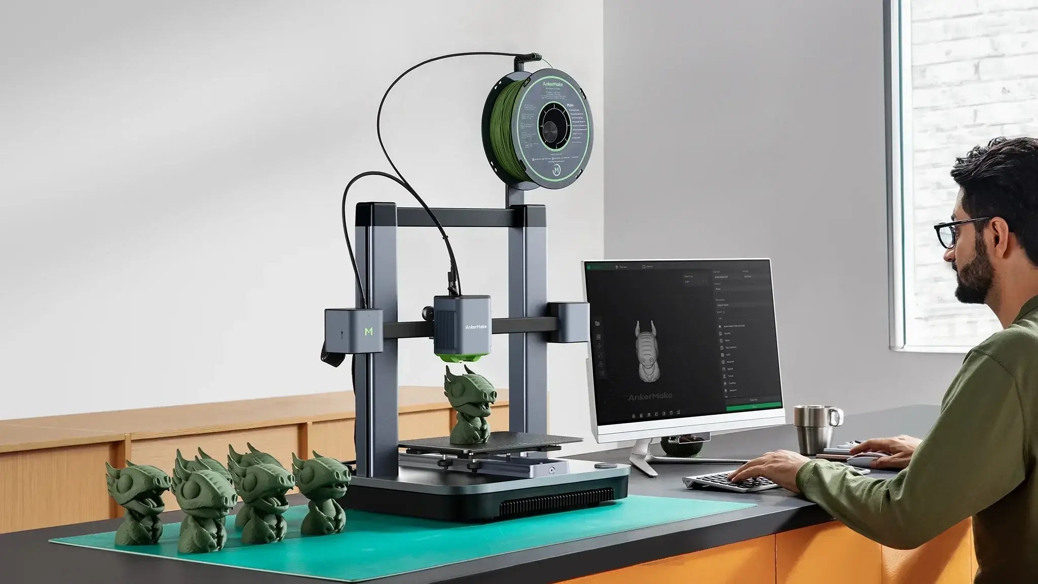 AnkerMake M5C-B 3D Printer on a desk printing detailed models with computer setup in the background.