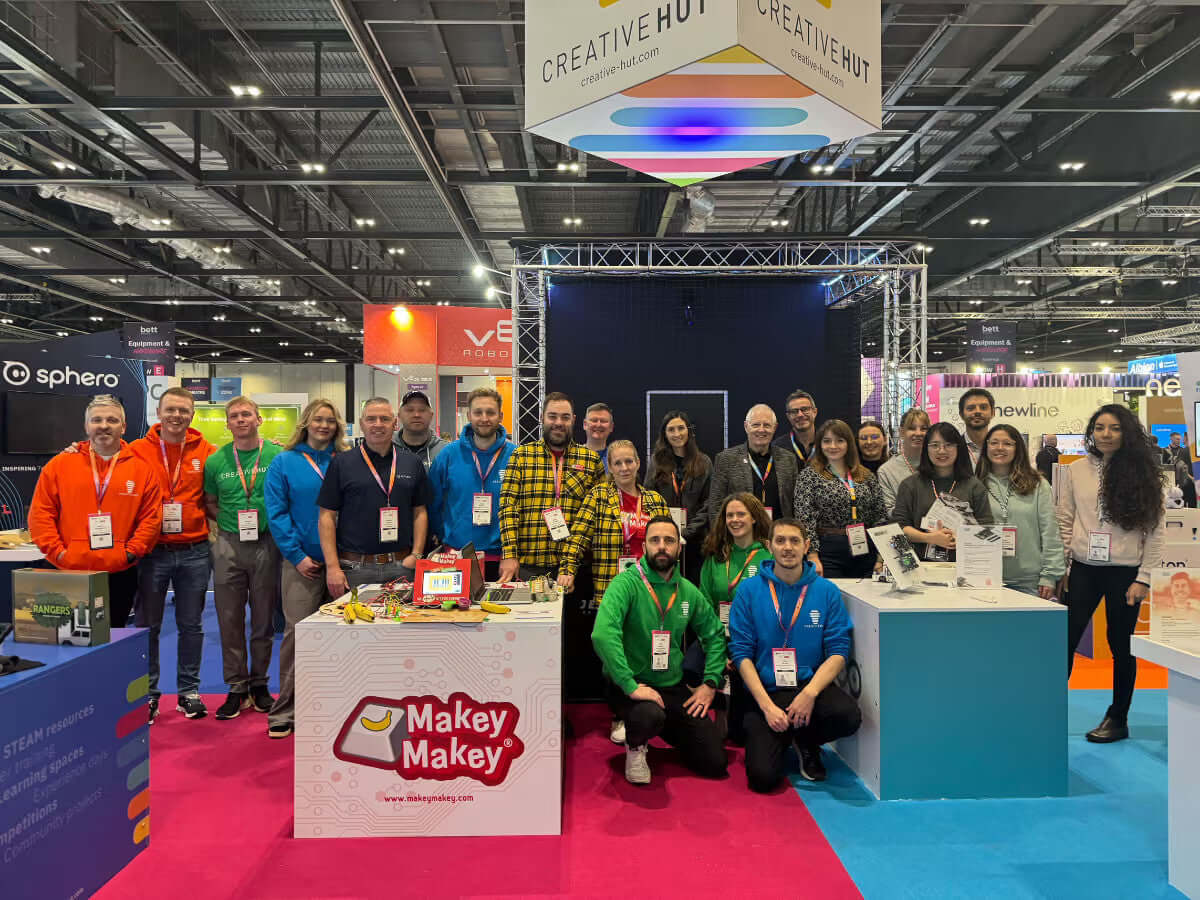 Group photo of attendees at the Creative Hut booth, showcasing Makey Makey and vibrant exhibition environment.