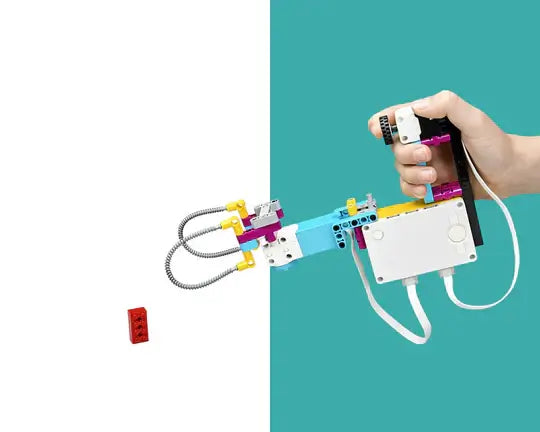 Hand holding a colorful robotic arm made of building blocks, aiming at a small red block on a contrasting background.