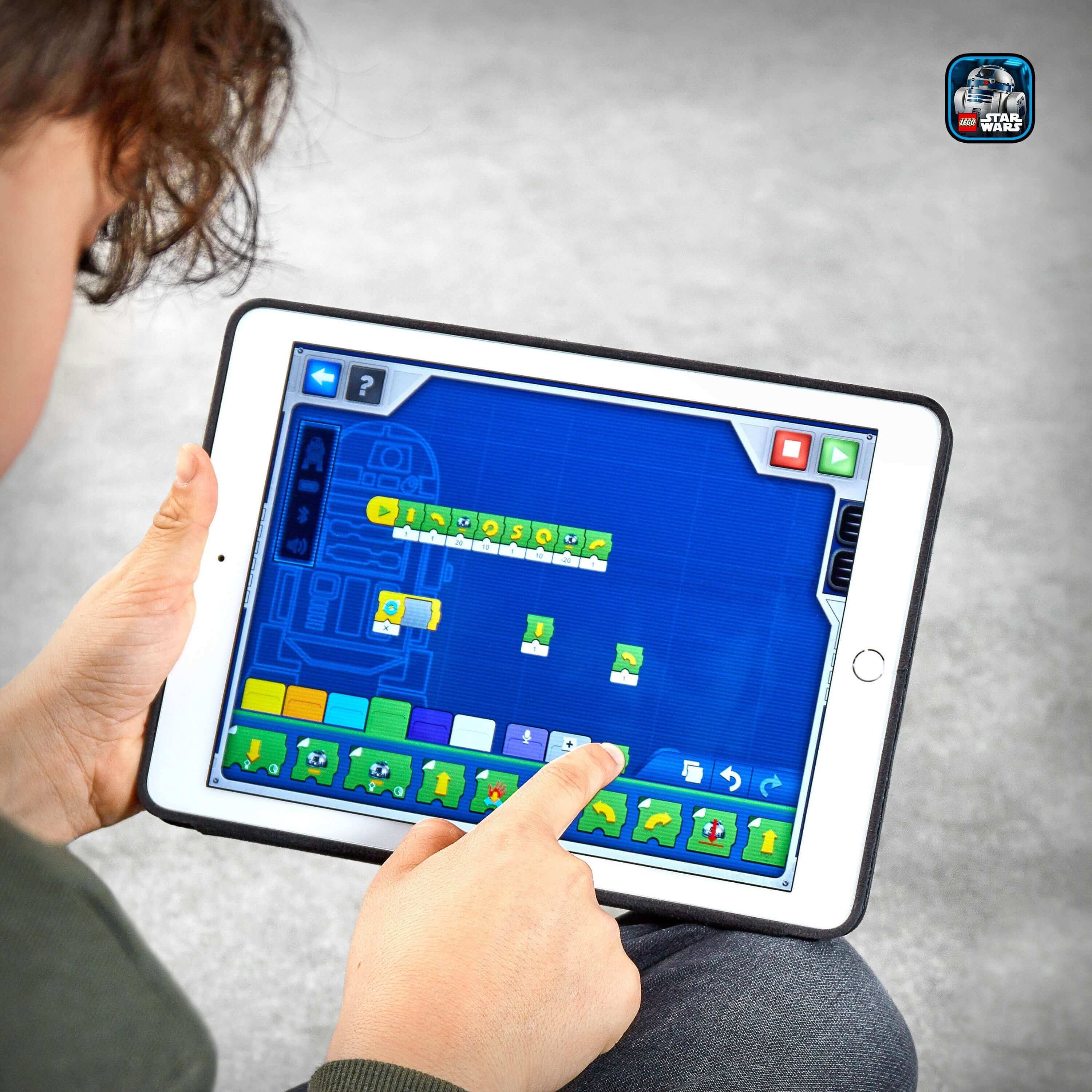 Child coding with LEGO Star Wars BOOST Droid Commander app on a tablet, controlling droid robots.