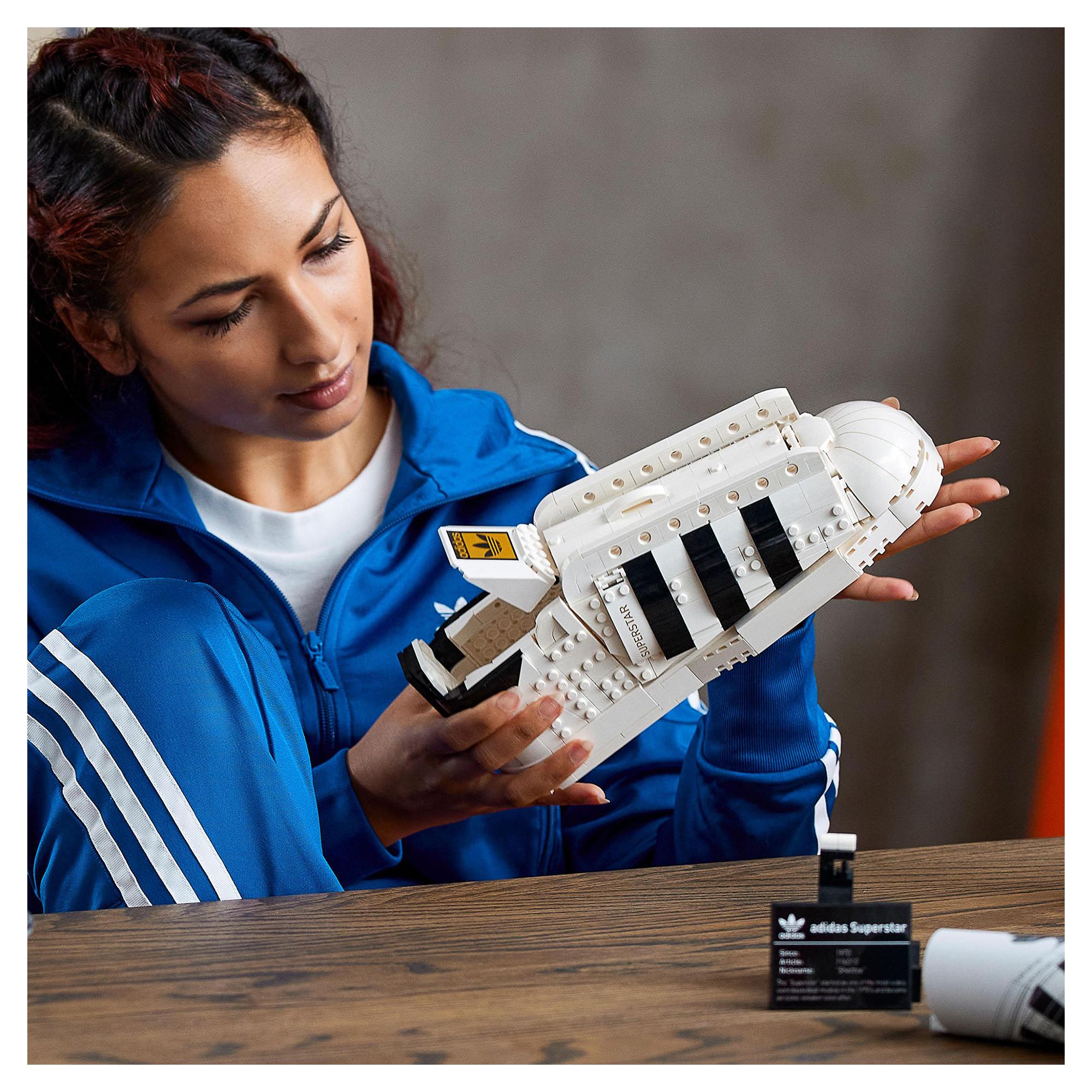 A person holds the LEGO® adidas Originals Superstar Set, showcasing the iconic trainer design with white and black details.