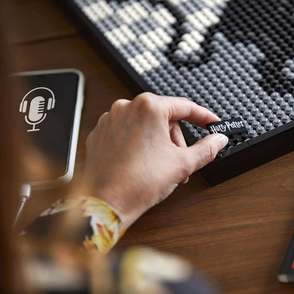 Person assembling LEGO® Art Harry Potter Hogwarts Crests set with a mobile device and immersive soundtrack.