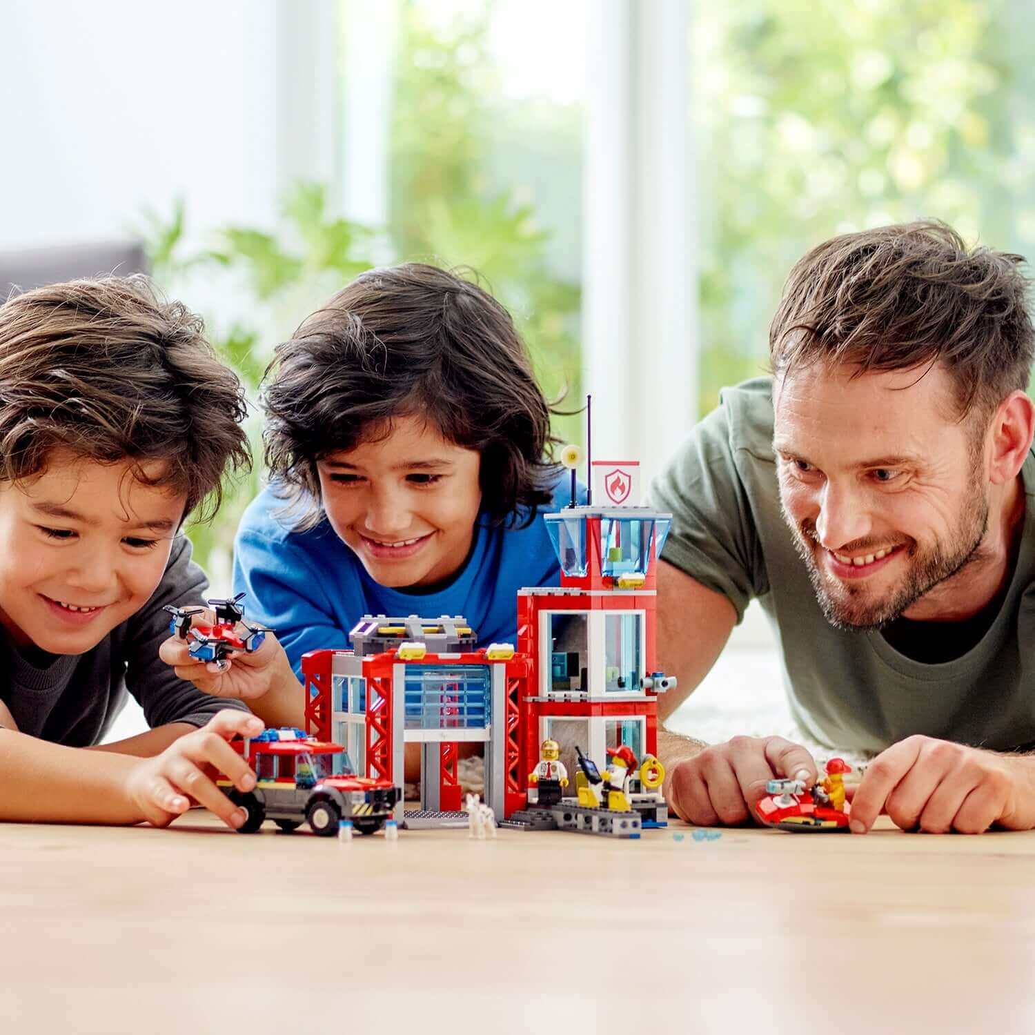 Two children and a man enjoy playing with LEGO® City Fire Station Truck Toy 60215, showcasing creativity and teamwork.