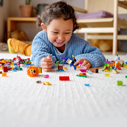 A happy child playing with colorful LEGO® pieces on the floor, showcasing creativity with transparent bricks from LEGO® Classic.