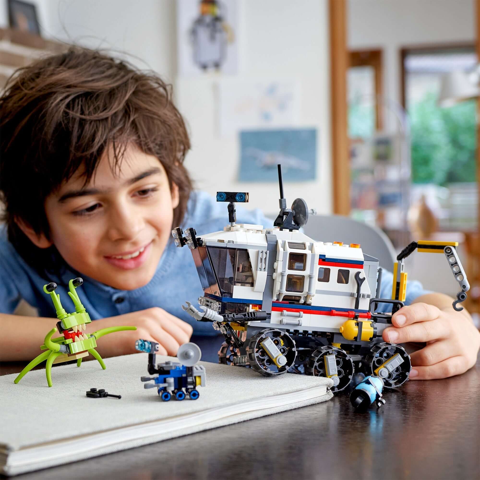 A young boy playing with the LEGO® Creator 3in1 Space Rover Explorer set, featuring a rover, alien figure, and space equipment.