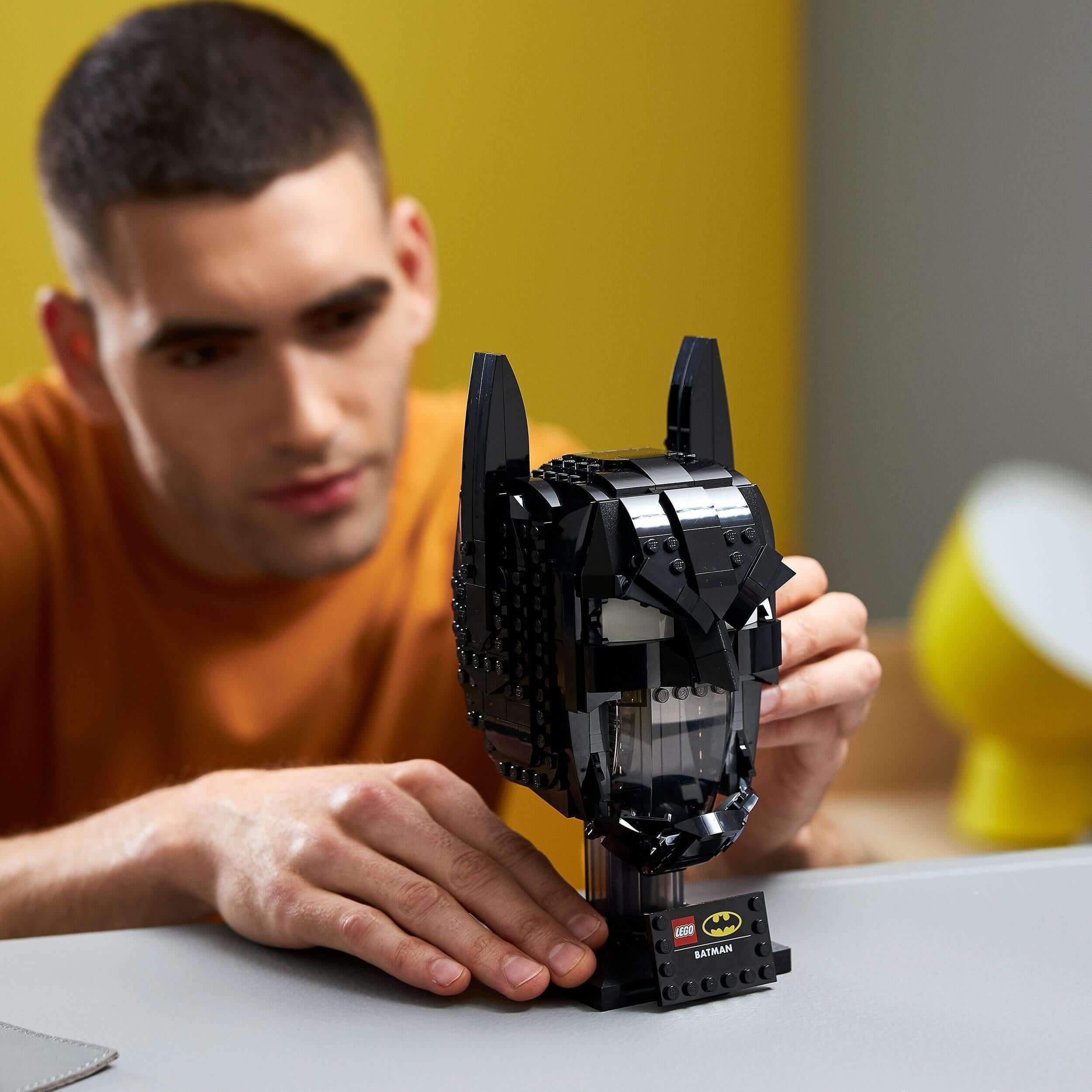 Adult man assembling the LEGO® Batman cowl set 76182, showcasing a detailed and immersive building experience.