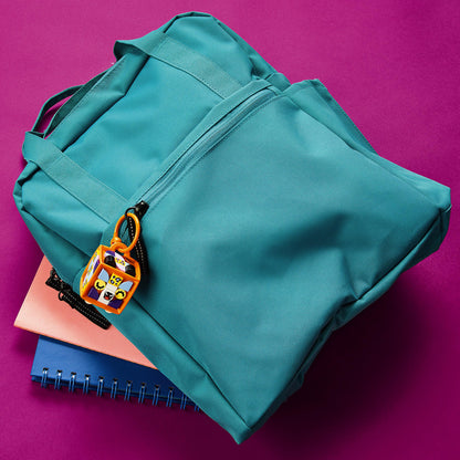 Teal backpack with a LEGO® DOTS Leopard bag tag, resting on colorful notebooks against a vibrant pink background.