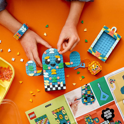 Child creating colorful LEGO® DOTS crafts: bracelet, bag tag, and picture frame on an orange surface.