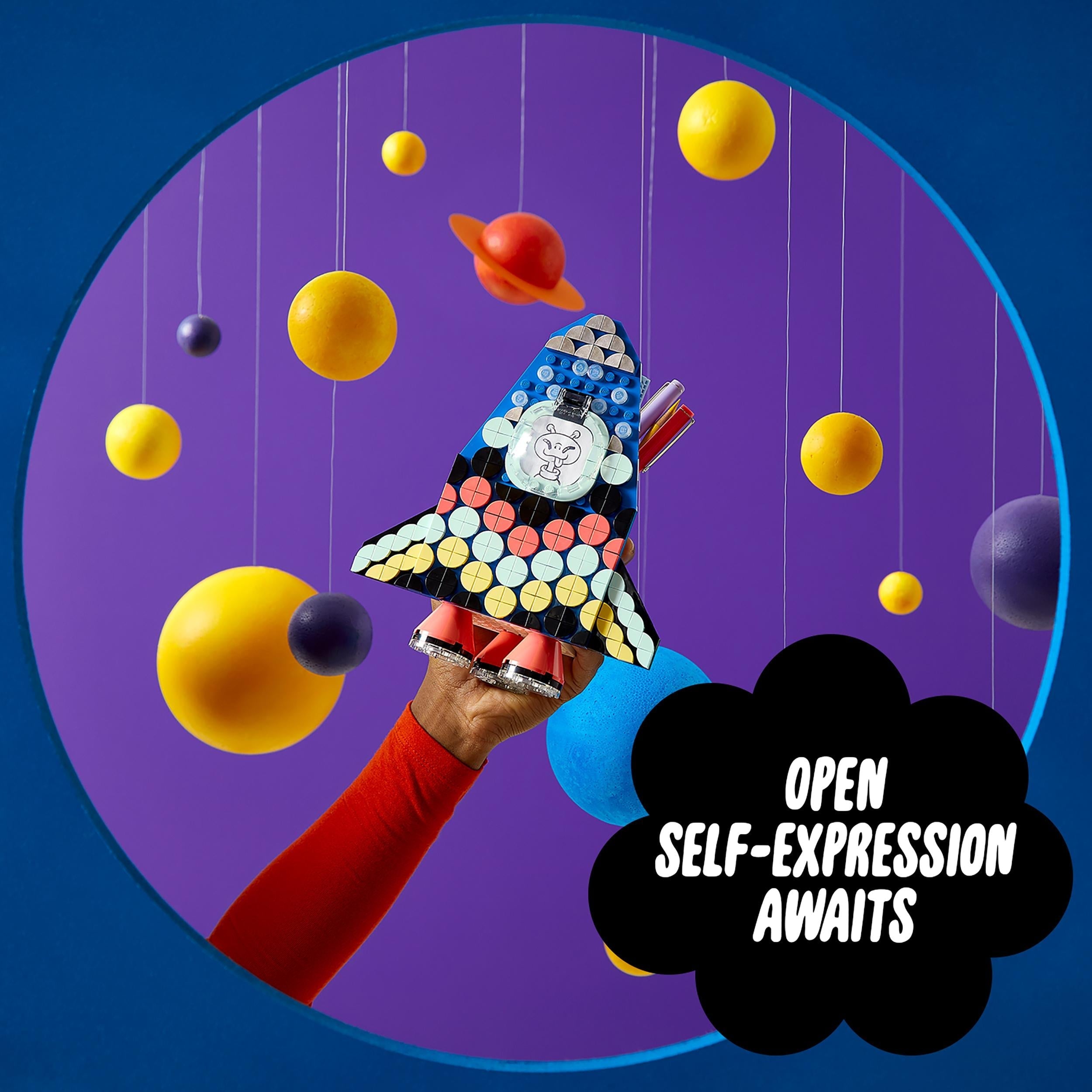 LEGO DOTS Pencil Holder Craft Set held up against a colorful planet backdrop, promoting creativity and self-expression for kids.