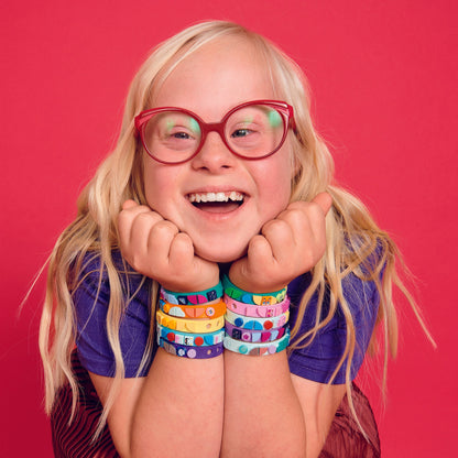 Child with colorful LEGO® DOTS starlight bracelets, smiling joyfully against a vibrant pink background.